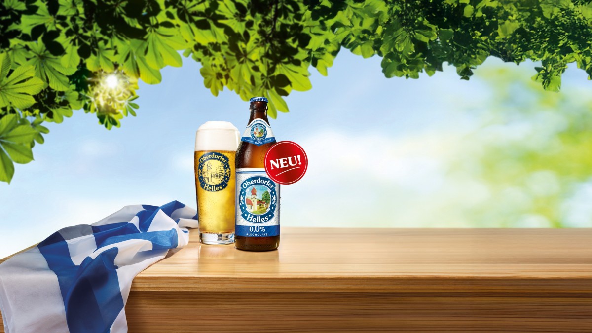 Zwei Bierflaschen neben gefüllten Biergläsern stehen auf einem Holztisch im Freien, umgeben von grüner Natur und Sonnenlicht.
